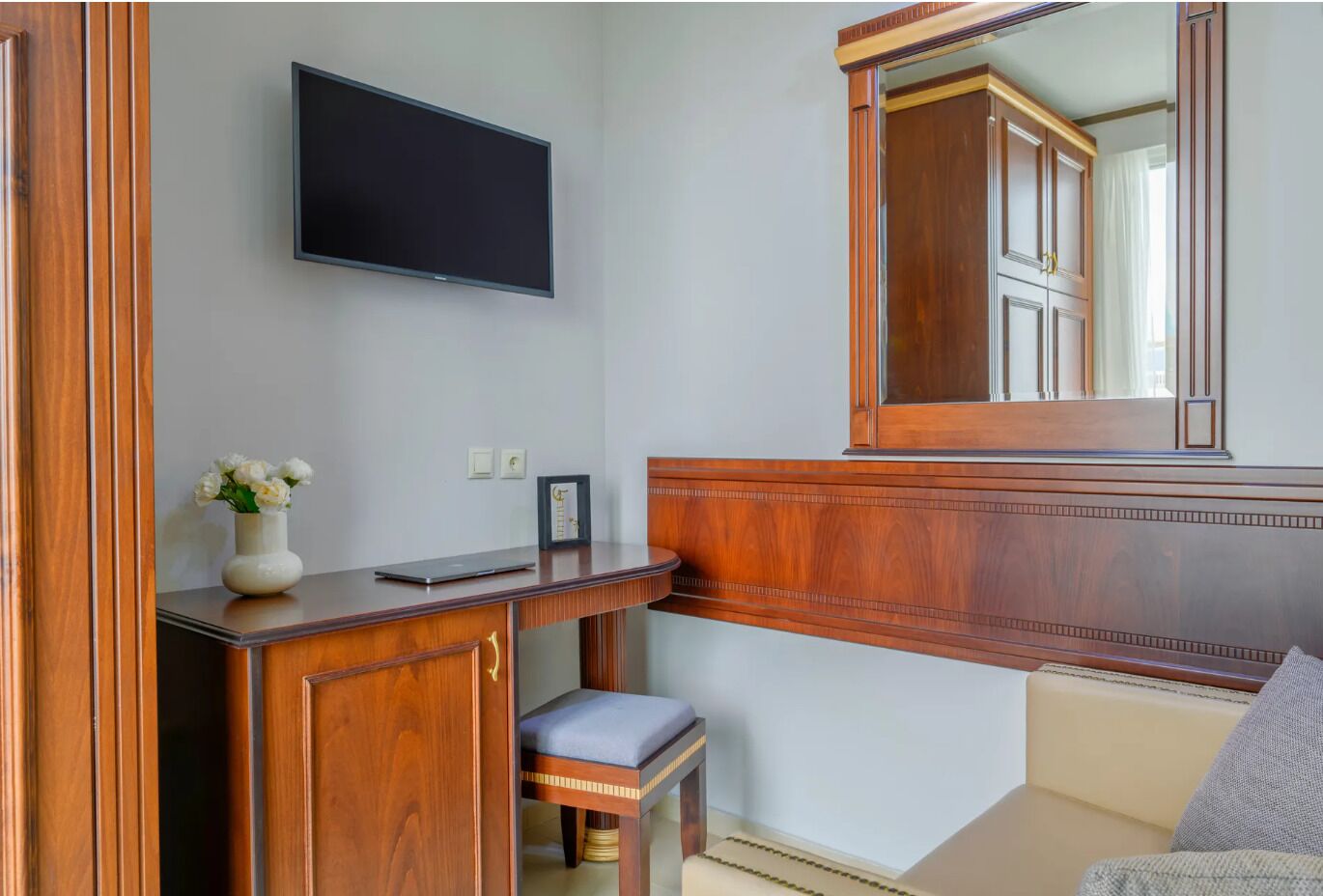 A wooden desk with a flat-screen TV, a vase with flowers, and a framed picture.