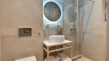 A modern bathroom with a glass-enclosed shower, a round mirror, and a white sink on a white shelf.