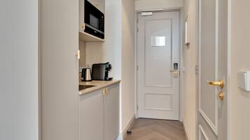 Ein schmaler Flur, der zu einer Tür mit kleinem Fenster führt, mit einer Mikrowelle über einer Arbeitsfläche und einer Kaffeemaschine auf der Arbeitsfläche.