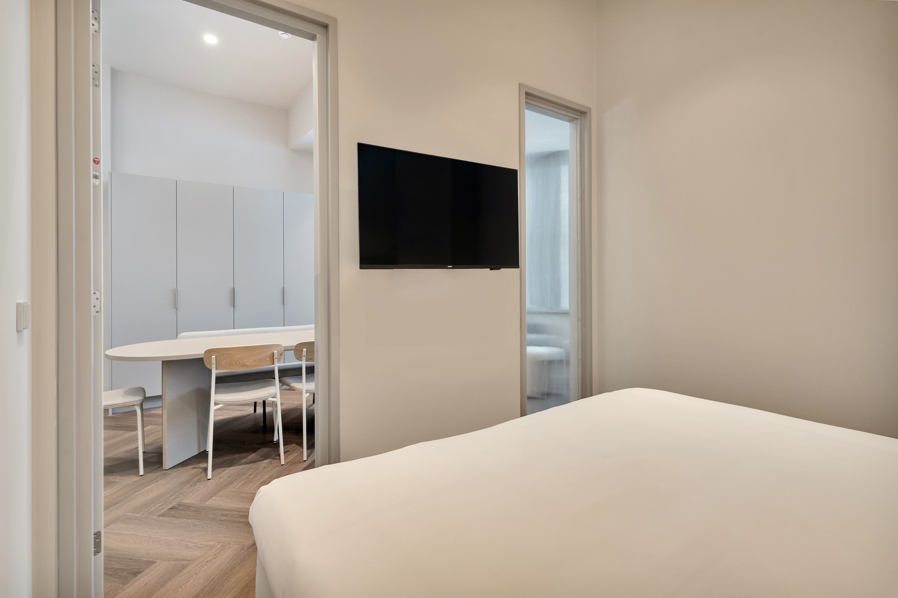 Une chambre à coucher avec un lit, un bureau avec une chaise et un téléviseur fixé au mur.