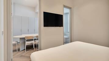 Une chambre à coucher avec un lit, un bureau avec une chaise et un téléviseur fixé au mur.