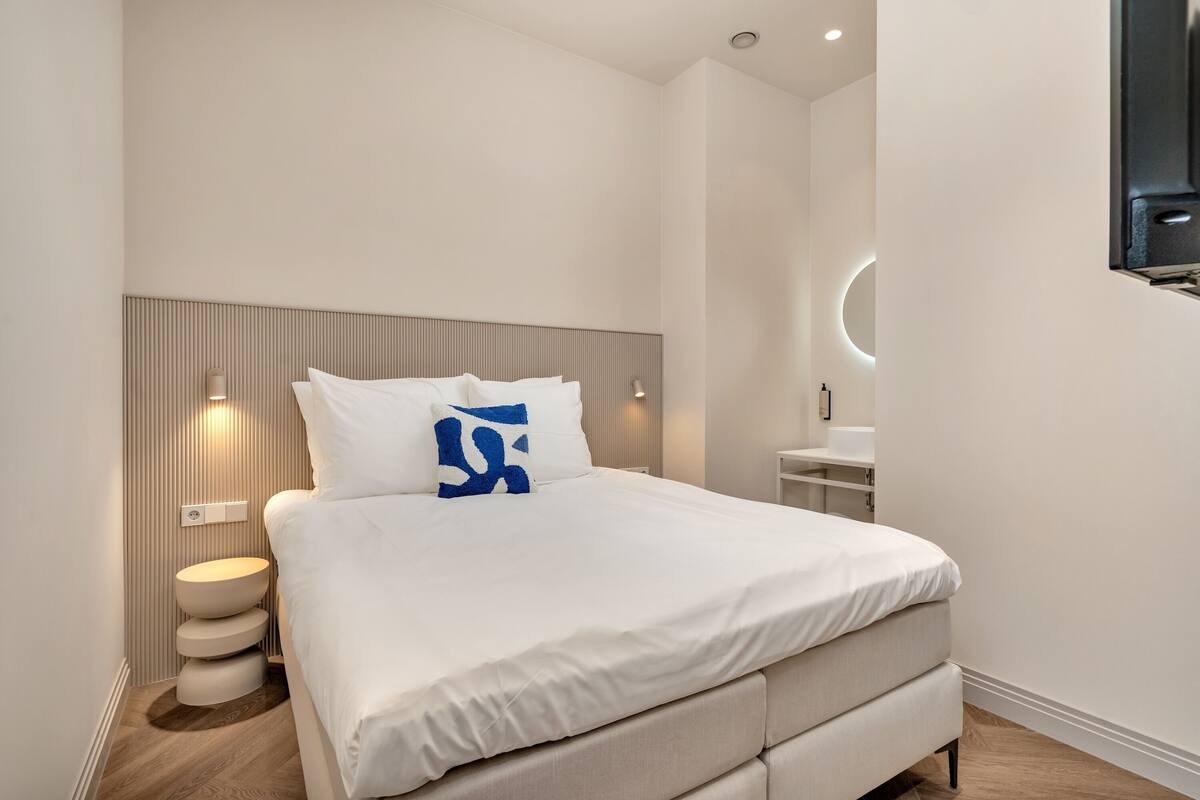 Ein modernes Schlafzimmer mit einem großen Bett, einem runden Nachttisch und einer Wandleuchte.