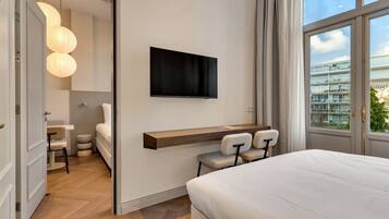 Una habitación de hotel moderna con cama, escritorio con sillas, televisor montado y un gran ventanal con vista a la ciudad.