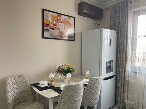 A dining area with a table set for two, a refrigerator, and a wall-mounted air conditioner. - Chaqar 50 (Tashkent)
