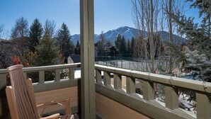 A wooden deck with a chair, overlooking a snowy mountain landscape with trees and a clear sky. - Condo with Fireplace and Mountain Views! Close to Sun Valley Village! (Sun Valley)