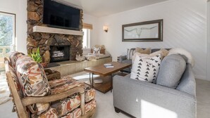 A living room with a stone fireplace, a flat-screen TV, a sofa, and a coffee table. - Condo with Fireplace and Mountain Views! Close to Sun Valley Village! (Sun Valley)