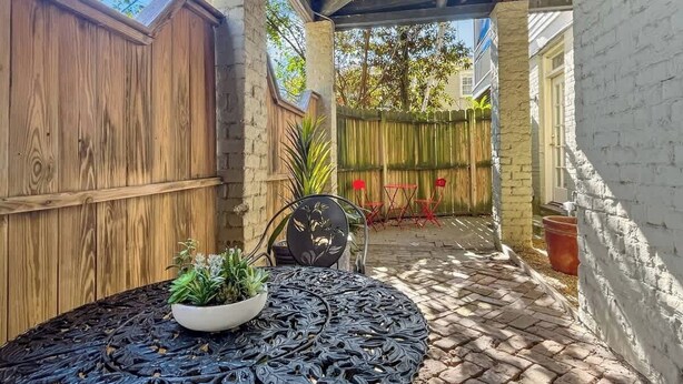 A covered patio area with a wooden fence, a brick wall, and a table with potted plants. - Historic Hideaway on Forsyth (Savannah)