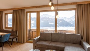 A room with a sofa, a dining table with chairs, and large windows with a mountain view. - Pleasant Apartment With Shared Sauna (Mittersill)