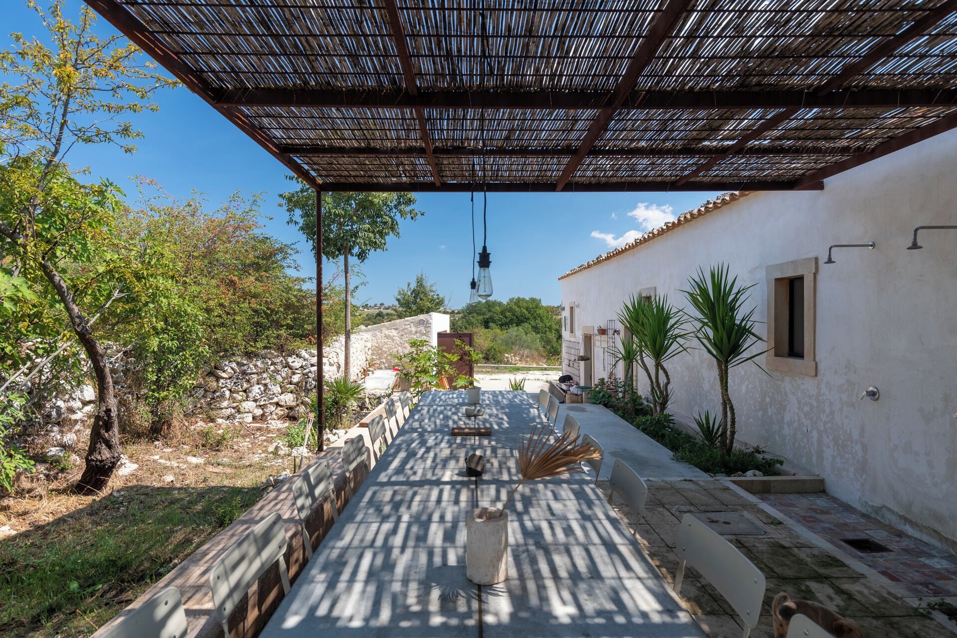 An outdoor dining area with a pergola, stone walls, and a view of the surrounding landscape.