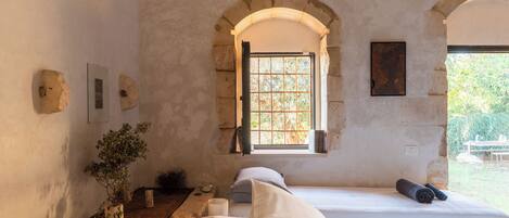 A rustic room with a large arched window, a wooden bench, and a bed with pillows.