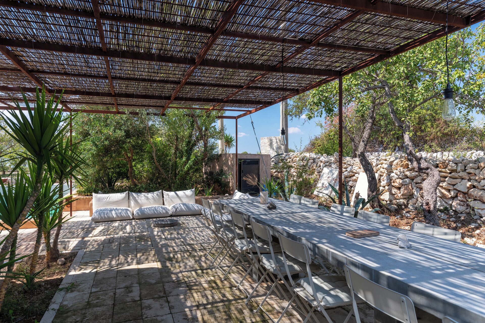 Un patio al aire libre con pérgola, paredes de piedra y mobiliario.