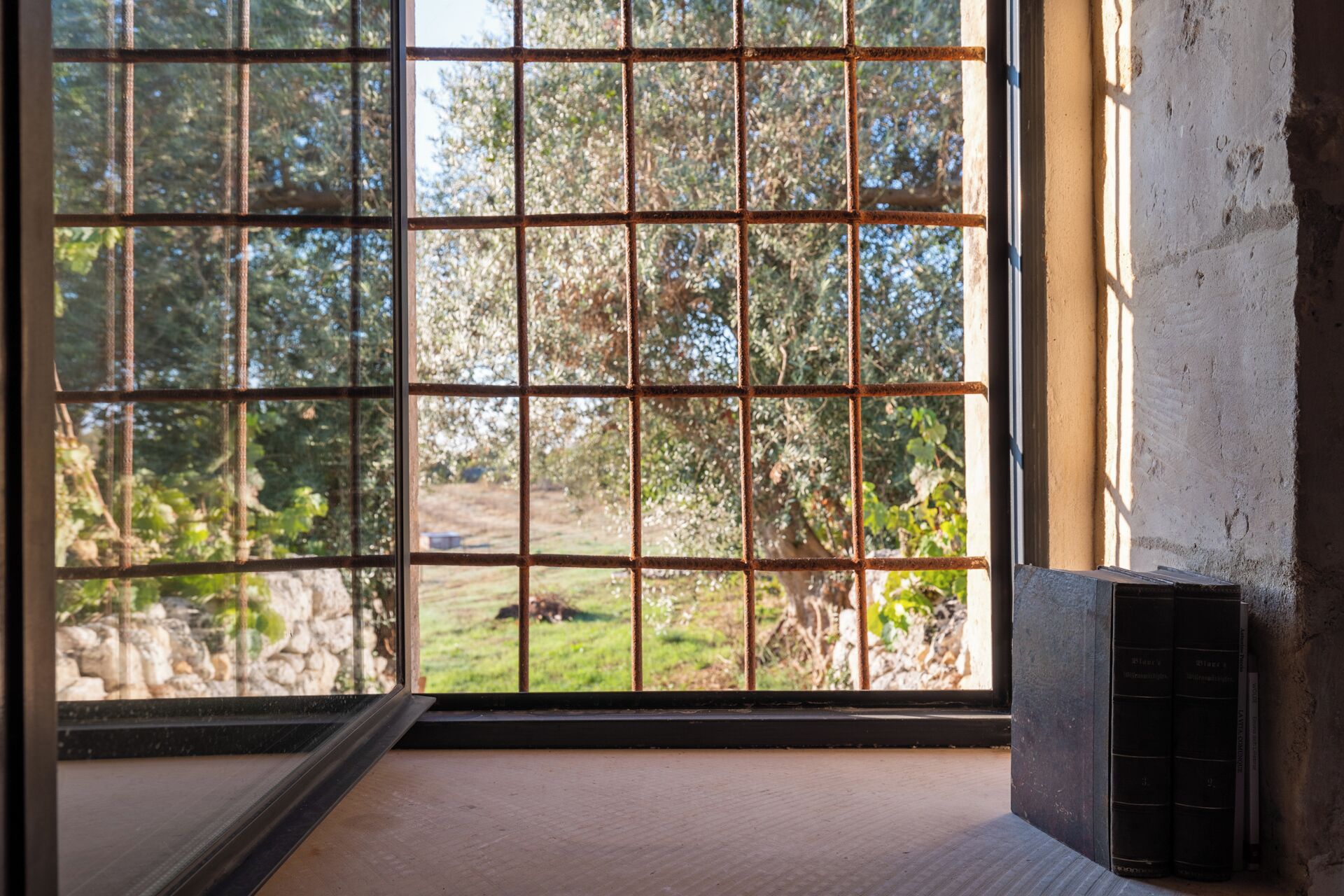 A room with a large window featuring a metal grid, a stone wall, and a radiator.