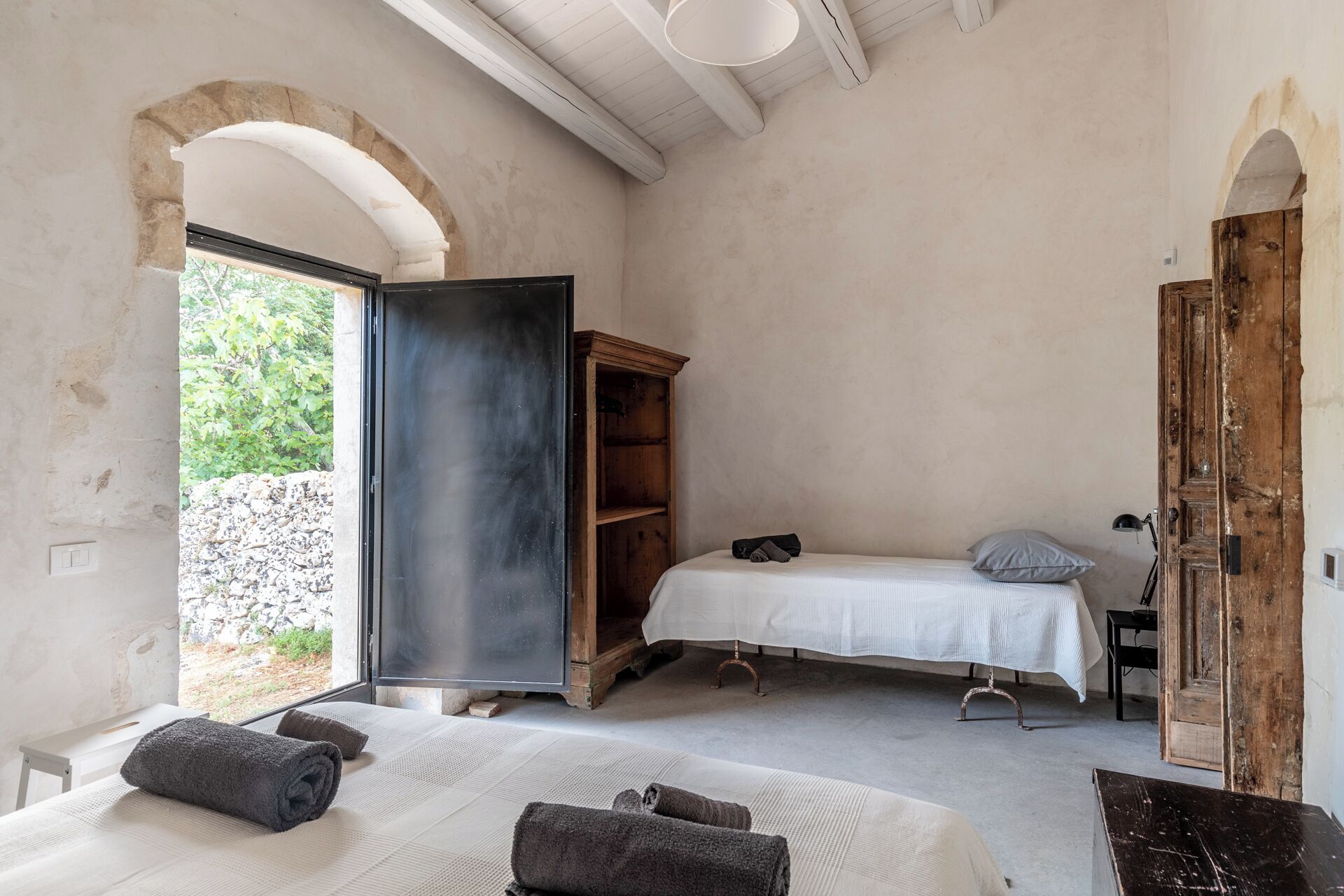Une chambre à coucher avec un lit, une armoire en bois, une petite table et une grande fenêtre en arc de cercle.