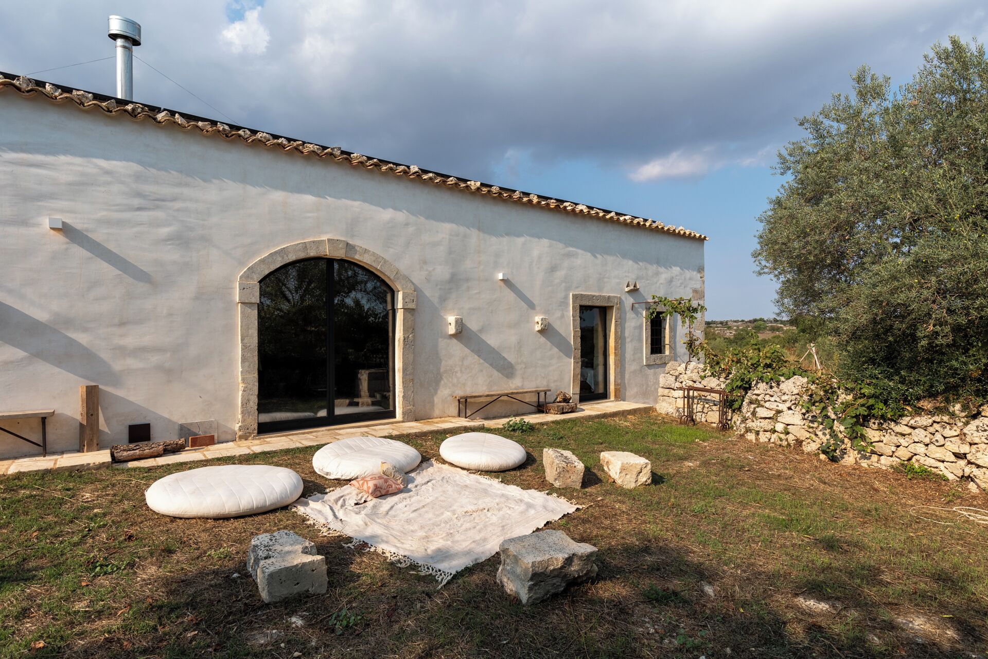 A rustic building with a stone facade, large arched windows, and a stone wall with vines.