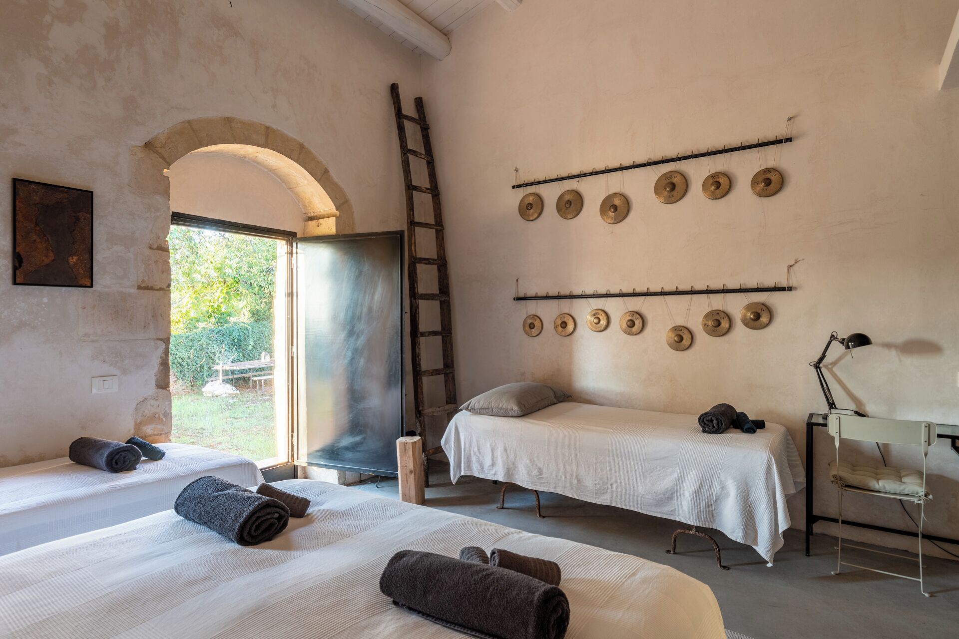 A room with two beds, a ladder, a wall-mounted cymbal rack, and a desk with a lamp.