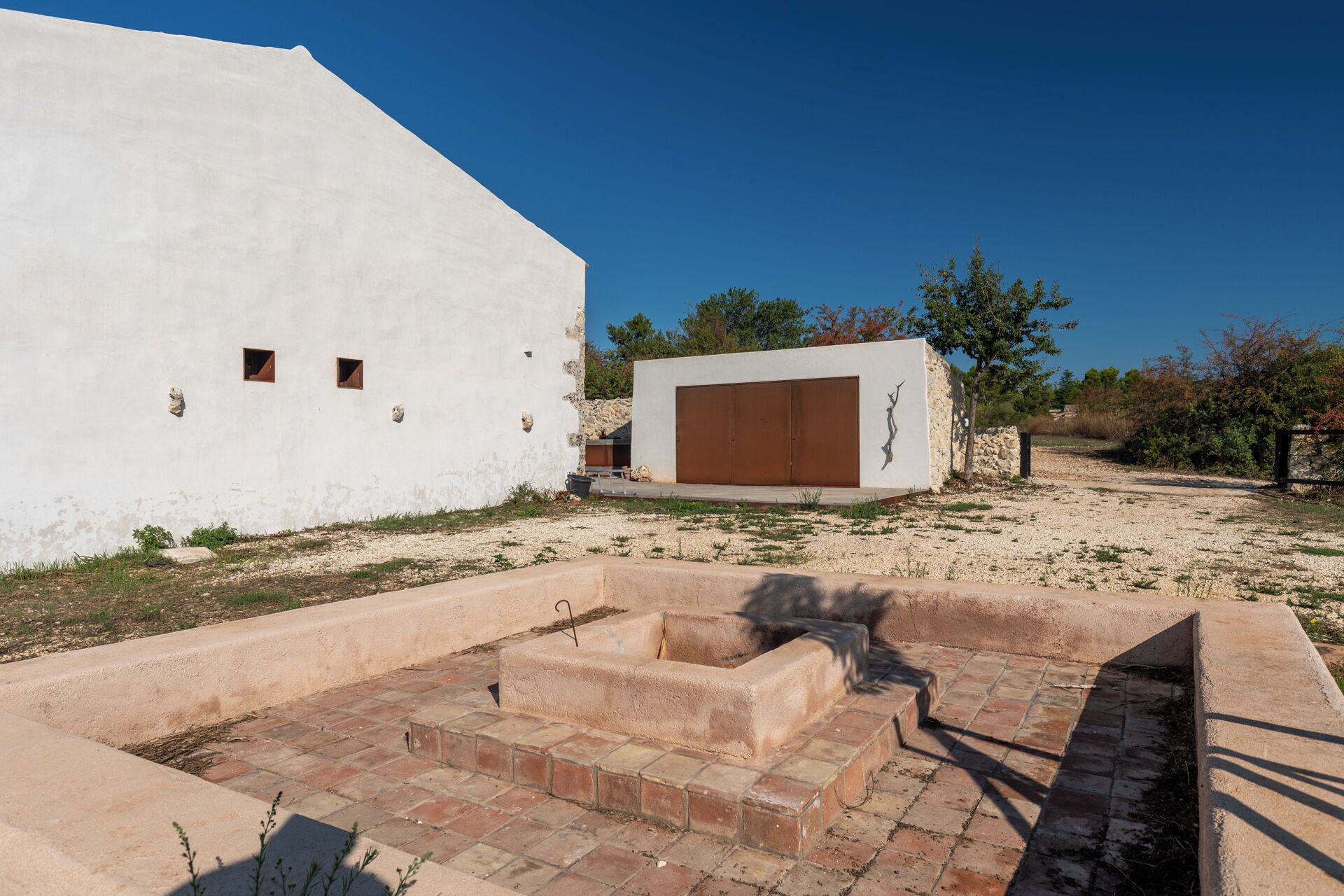 A white building with a large brown door, a small window, and a stone wall.