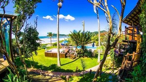A tropical resort with a pool, lounge chairs, and a view of the ocean. - Pousada Canto da Vigia (Penha)