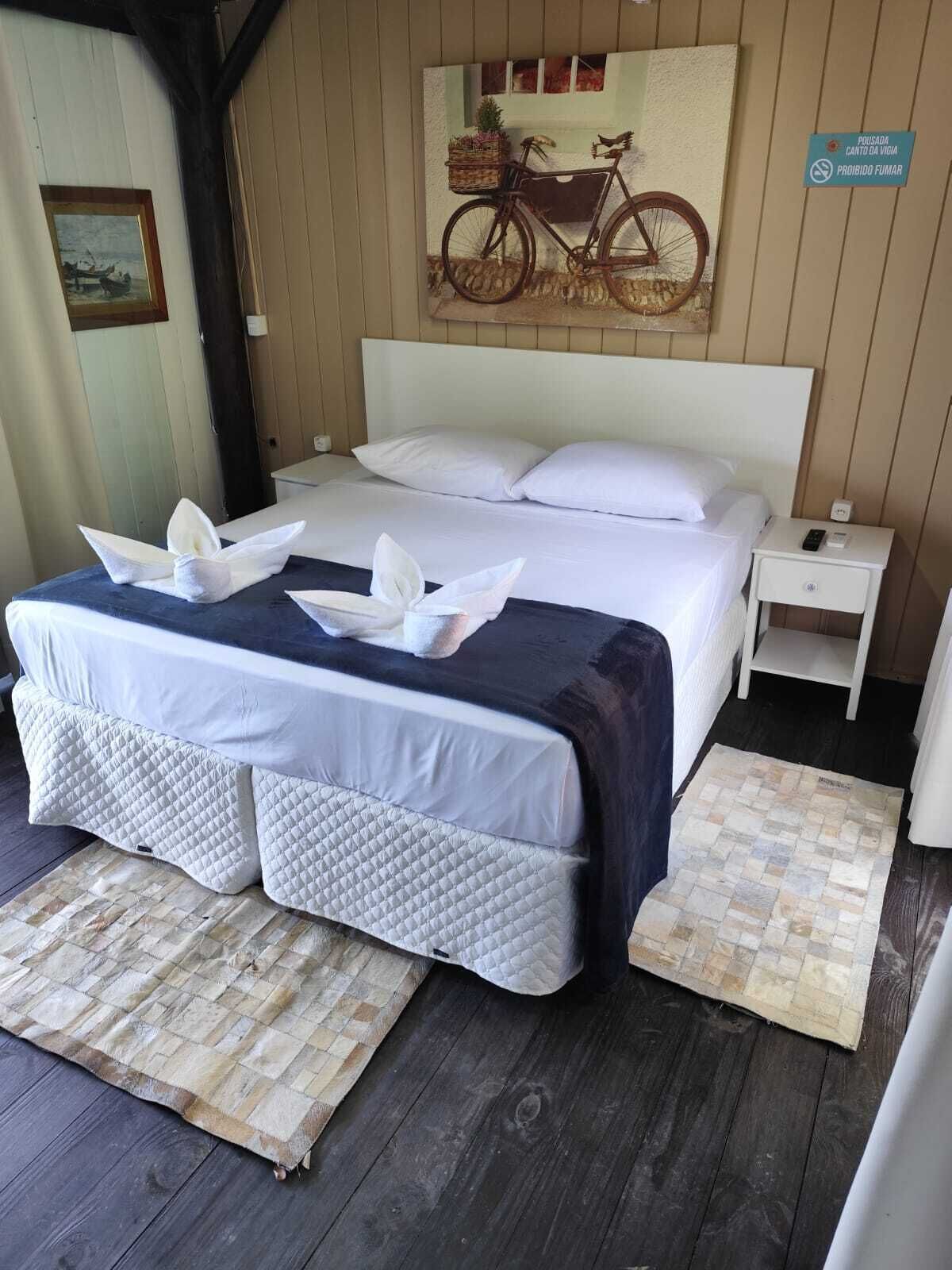 A neatly made bed with white linens and two decorative pillows, a small bedside table with a lamp, and a wall-mounted sign indicating a smoking area.