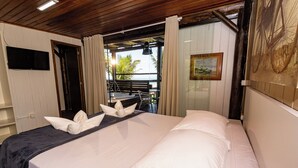 A hotel room with a bed, white pillows, a flat-screen TV, a painting, and a view of the outdoors. - Pousada Canto da Vigia (Penha)