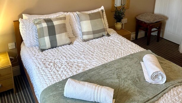 A neatly made bed with a rolled towel, a bedside table with a lamp, and a small chair. - Wellington Studio, Sleeps 2, Pets Ok, Free Parking (Northallerton)