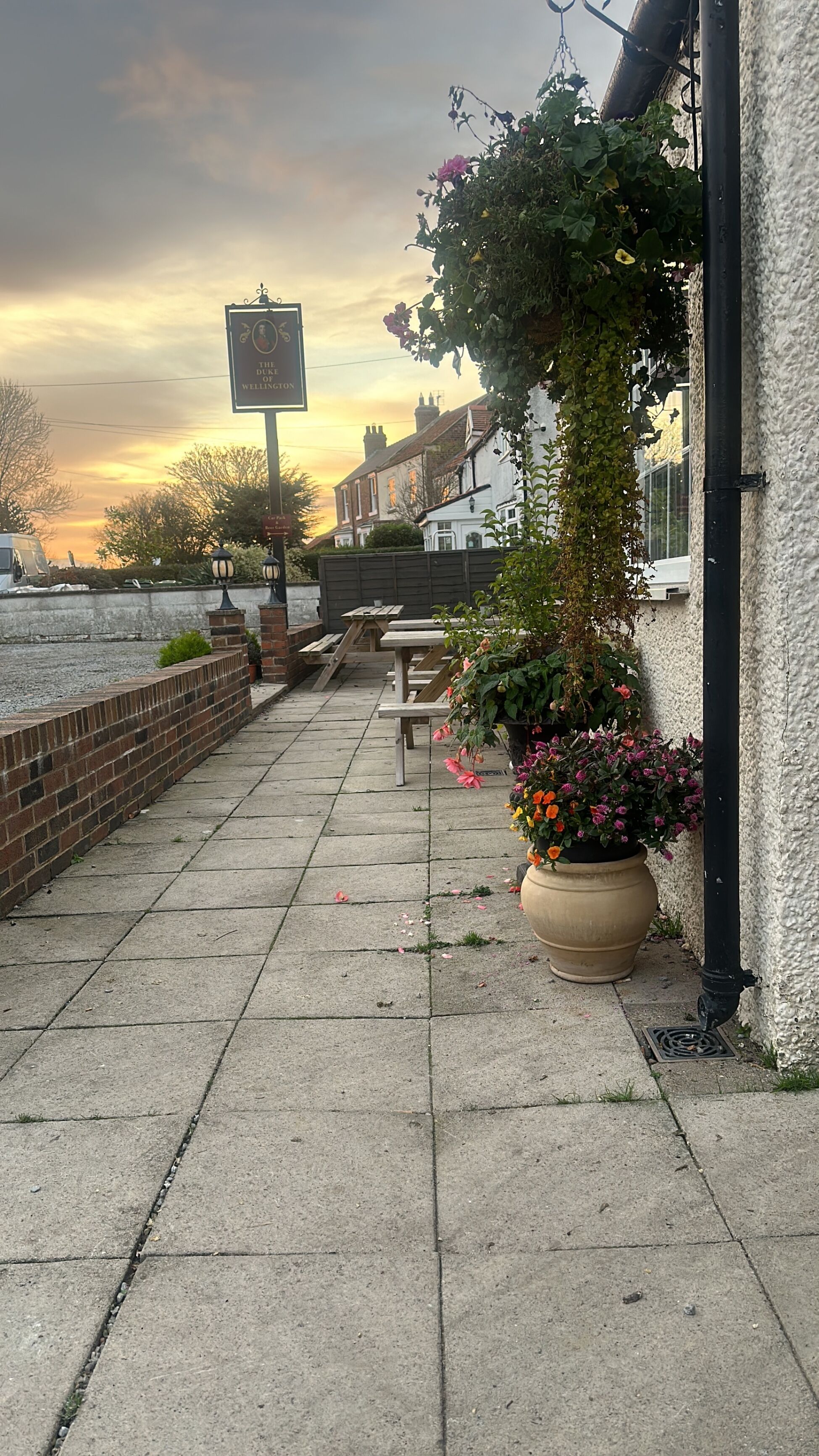 Un patio con pared de ladrillo, un letrero que dice "The Duke of Wellington" y mobiliario para estar al aire libre.