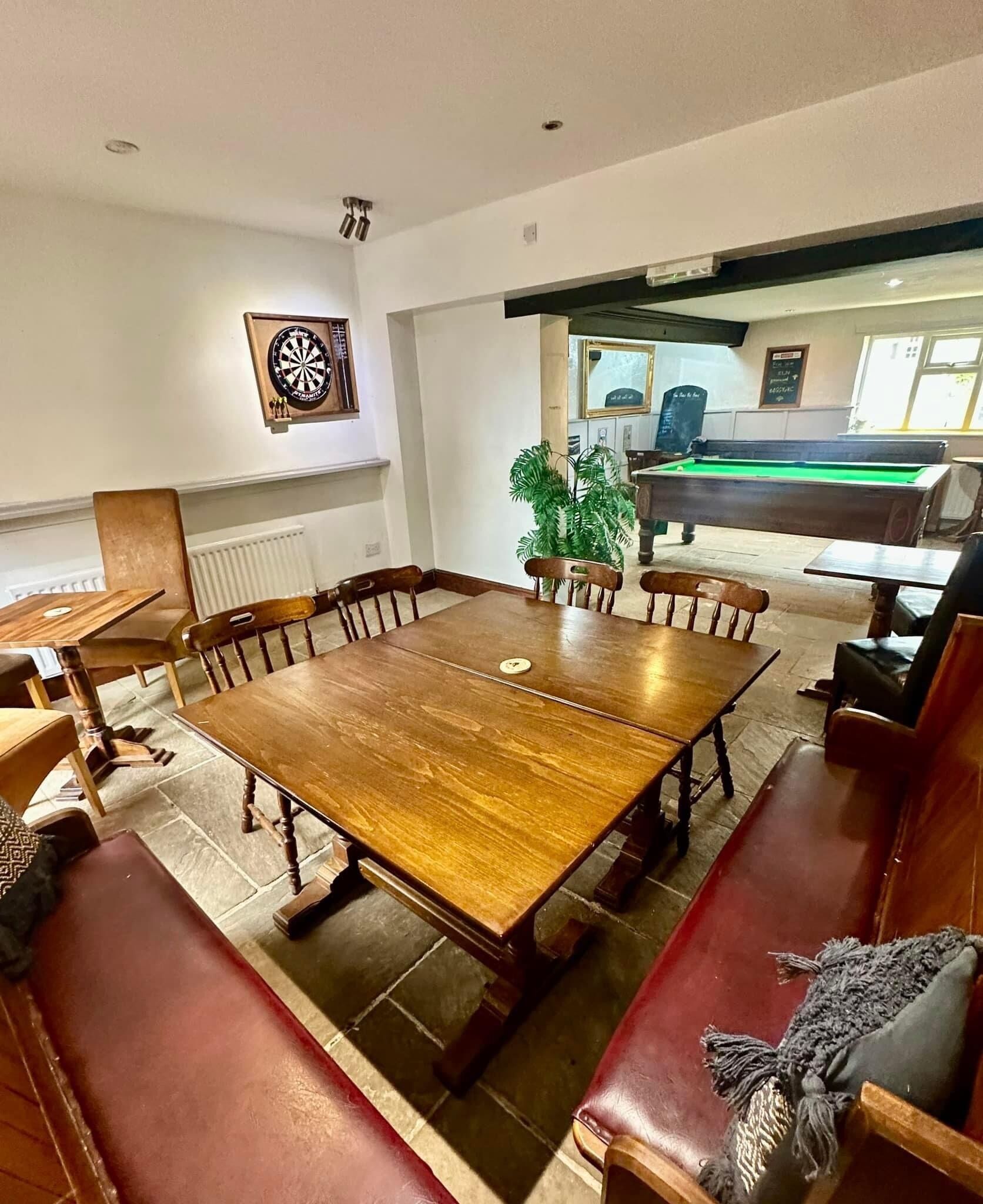 A spacious room with a large wooden table surrounded by leather benches, a dartboard, and a billiards table.