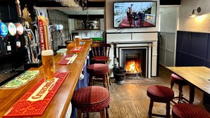 A bar area with a fireplace, stools, and a television screen displaying an outdoor scene. - Wellington Studio, Sleeps 2, Pets Ok, Free Parking (Northallerton)