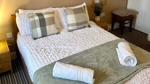 A neatly made bed with a checkered pillow, a rolled towel, and a green blanket. There is a small stool and a mirror on the wall. - Wellington Studio, Sleeps 2, Pets Ok, Free Parking (Northallerton)
