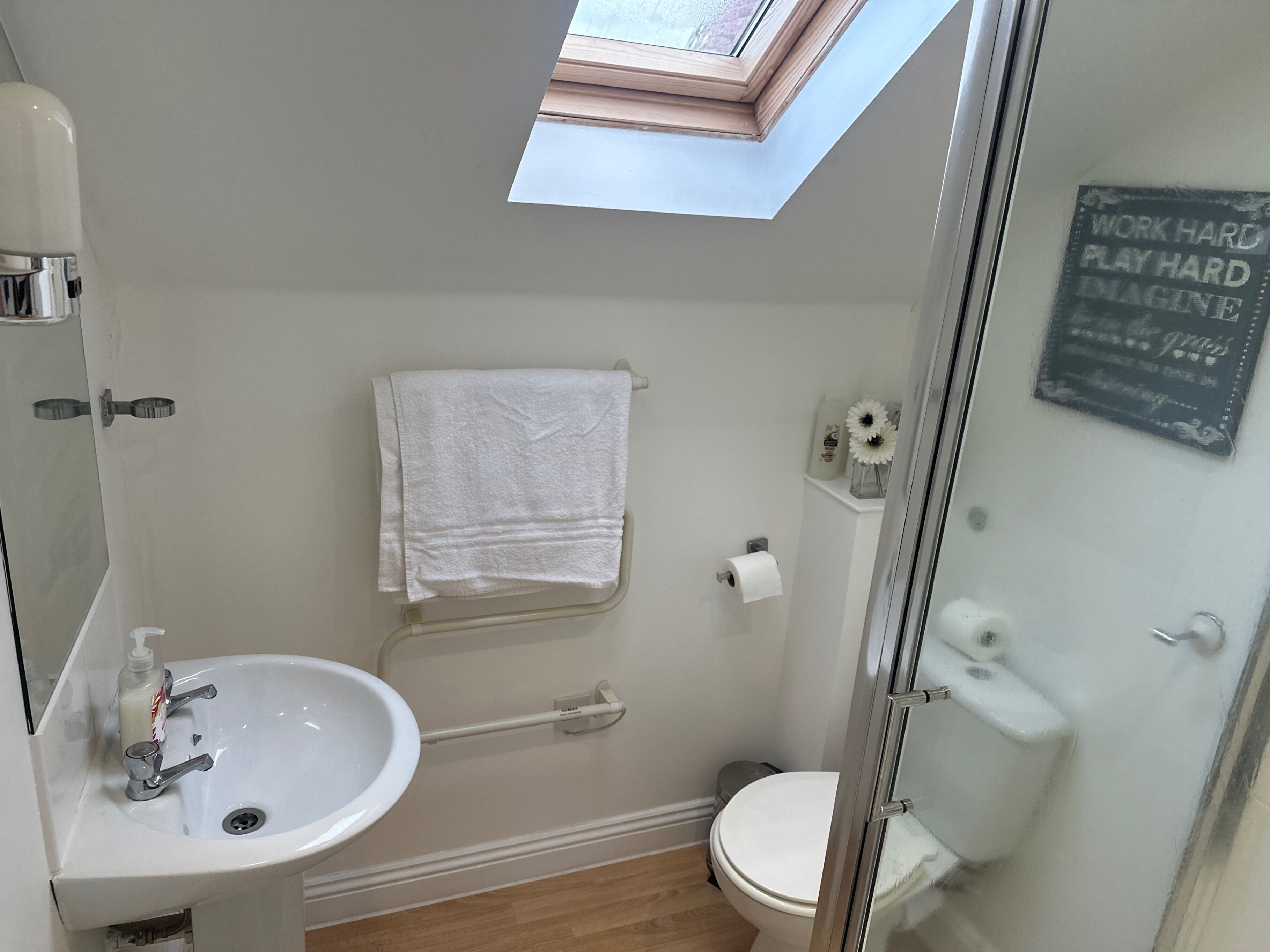 Une salle de bain avec un puits de lumière, un lavabo, des toilettes et une serviette accrochée au mur.