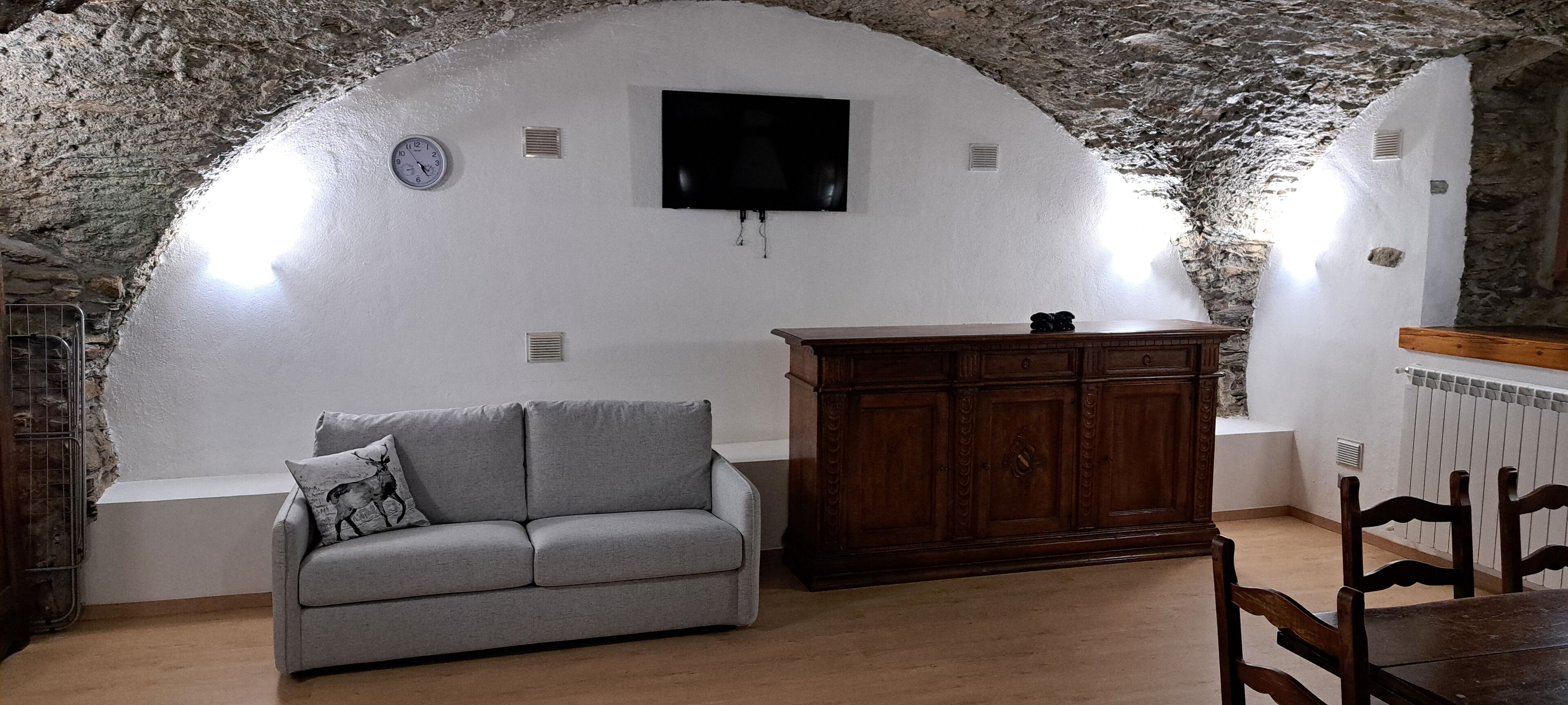 Une pièce chaleureuse avec un plafond en pierre, un canapé gris, un meuble en bois et une table à manger avec des chaises.