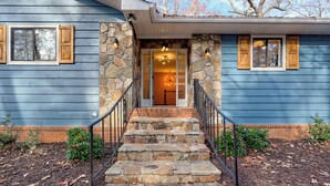 A house with a stone staircase leading to a wooden door, surrounded by a brick foundation and stone walls. - Lakeside Therapy by Chatuge Home Concierge | Lakefront · Dock · Firepit · Ping Pong (Hiawassee)