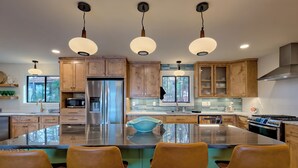A modern kitchen with wooden cabinets, stainless steel appliances, and a central island with bar stools. - Lakeside Therapy by Chatuge Home Concierge | Lakefront · Dock · Firepit · Ping Pong (Hiawassee)