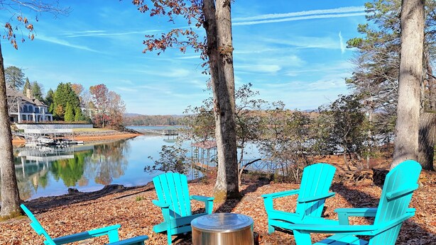 A lakeside seating area with turquoise Adirondack chairs and a metal fire pit. - Lakeside Therapy by Chatuge Home Concierge | Lakefront · Dock · Firepit · Ping Pong (Hiawassee)