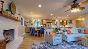 A modern living room with a fireplace, a dining area, and a kitchen with wooden cabinets and a large island. - Lakeside Therapy by Chatuge Home Concierge | Lakefront · Dock · Firepit · Ping Pong (Hiawassee)