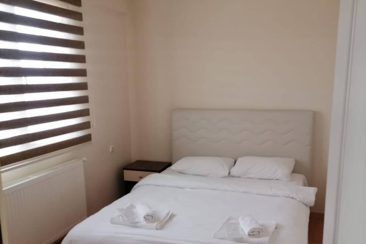 Un lit bien fait, avec du linge de lit et des serviettes blanches, un plancher en bois et une fenêtre avec des stores.