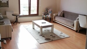 A living room with a sofa, a coffee table, a chair, a radiator, and a window with a view. - Snow Life Hotel Sarıkamış (Sarikamis)