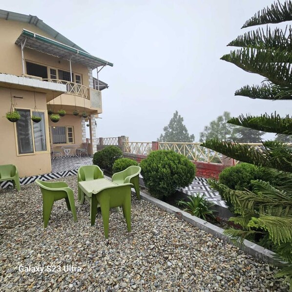 A building with a balcony, outdoor seating area with green chairs, and a patterned floor.