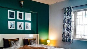 Un dormitorio con cama, mesita de noche, lámpara y ventana con cortinas.