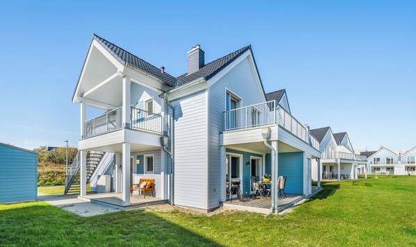 Una casa de dos pisos con balcón, porche cubierto y una escalera visible.