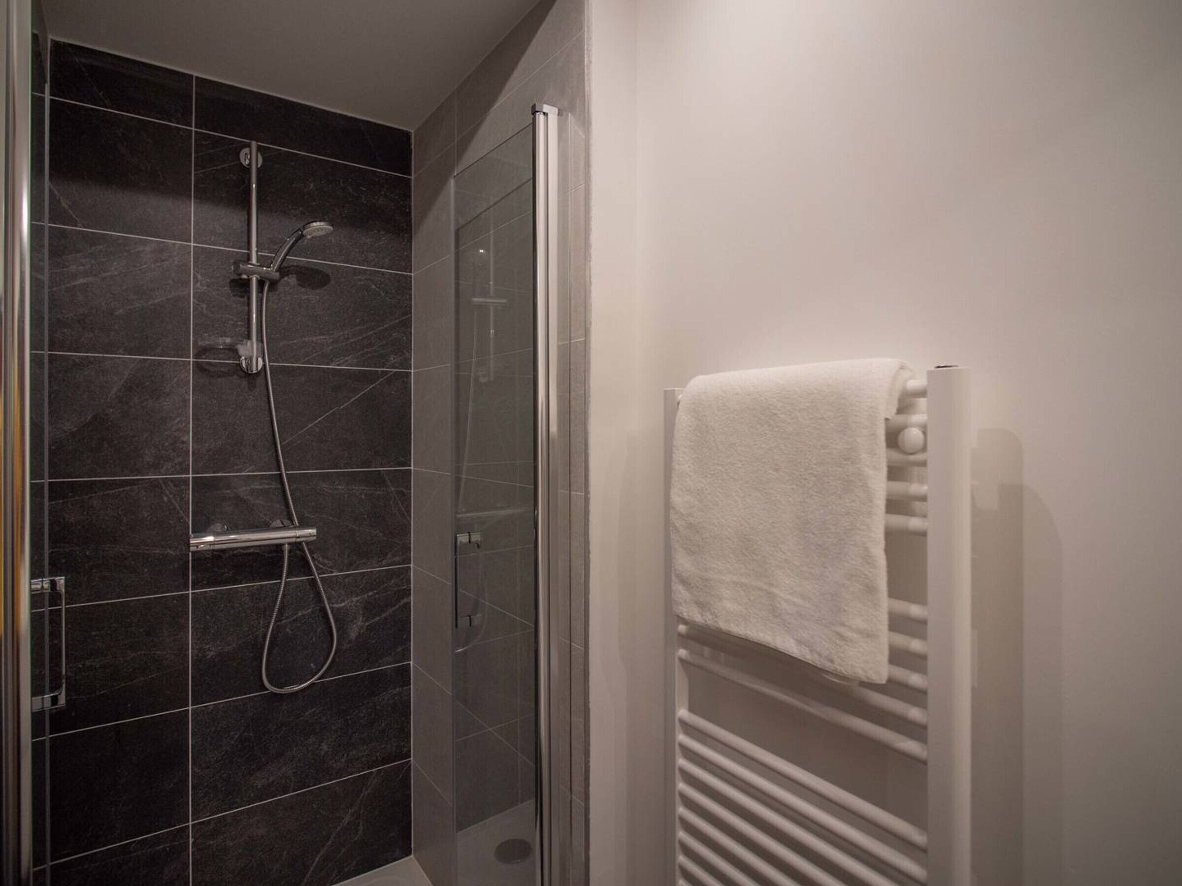 A modern bathroom with a glass-enclosed shower, a white towel rack, and a tiled floor.