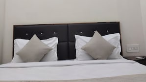 Quarto de hotel com cama, duas almofadas, mesa de cabeceira e criado-mudo.