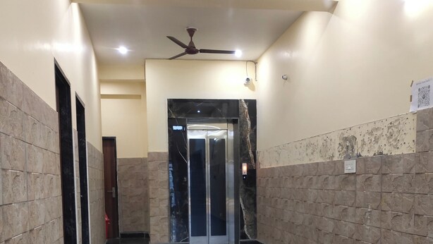 Um corredor com piso de mármore, ventilador de teto e elevador.