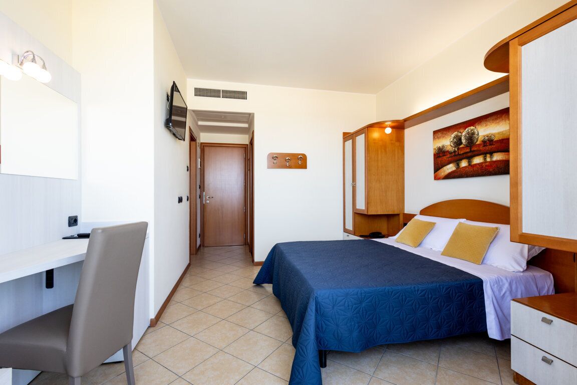 Habitación de hotel con cama, escritorio y silla. Hay un cuadro en la pared y una puerta que da a otra habitación.