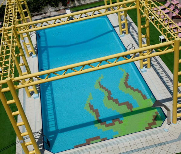 A swimming pool with a yellow safety structure and a green and brown patterned deck. - Hotel Palm Beach (Rimini)