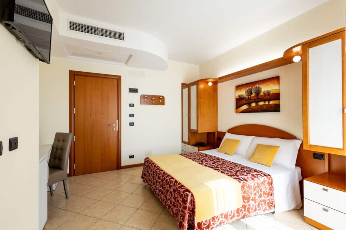 A hotel room with a bed, bedside table, chair, and a painting on the wall.