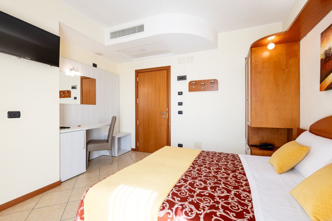 A hotel room with a bed, a desk, a chair, a TV, and a wardrobe.