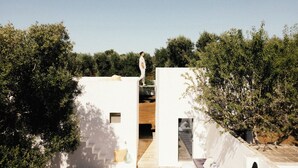 Eine Person steht auf einem Balkon eines weißen Gebäudes, von dem eine Treppe zu einer höheren Ebene führt.