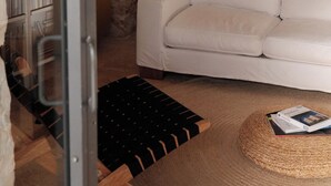 Ein Zimmer mit einer Steinswand, einem weißen Sofa, einem schwarzen Holzstuhl und einem gewebten Teppich.