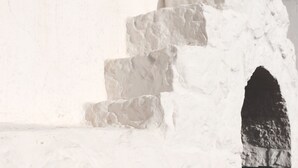 Eine weiße Steintreppe führt zu einer dunklen Türöffnung, Teil eines Gebäudes mit schlichter Fassade.