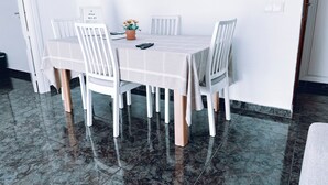 A dining area with a table set for four, white chairs, a vase with flowers, and a remote control on the table. - Aperol Apartment - Malaga (Málaga)